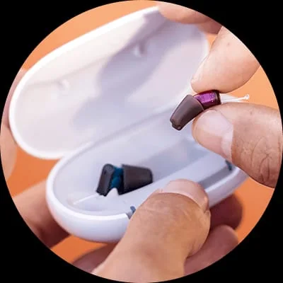 Small in-ear hearing aid being handled near a charging case